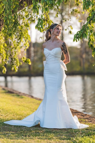 Bride in strapless mermaid gown standing by the waterfront under weeping willow branches in golden afternoon light
