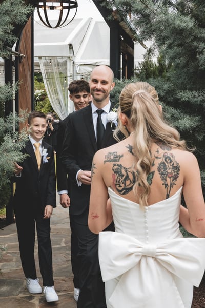 Groom beaming at the bride as she approaches for their first look, with two young groomsmen looking on delightedly