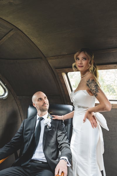 Bride kneeling gracefully beside the seated groom inside the vintage aircraft cabin, her hand on his shoulder, both gazing upward in a tender moment