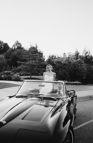Bride in reception dress standing in the open Corvette while groom sits at the wheel at dusk