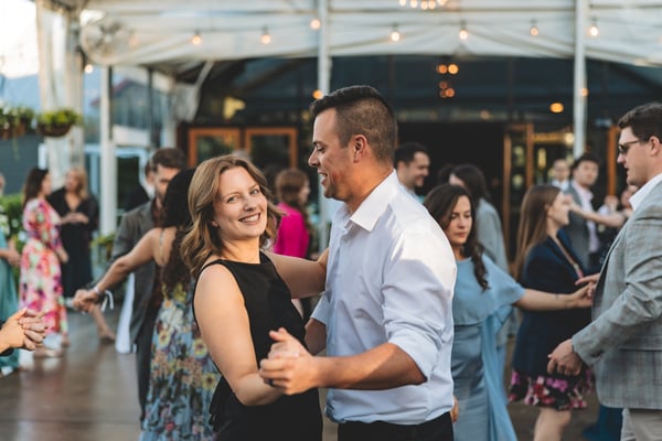 Guests filling the outdoor dance floor at dusk, couples dancing together under string lights on a tented patio