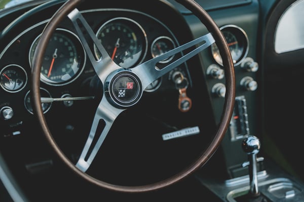 Close-up of a vintage Corvette steering wheel and dashboard instruments with wood trim and chrome accents