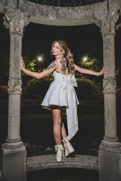 Bride in short white dress with arms spread wide in the night gazebo, bejeweled Converse on the stone steps, confidence and joy radiating