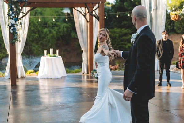 Bride laughing while spinning toward the groom on the outdoor dance floor at dusk, the altar and draped fabric visible behind them