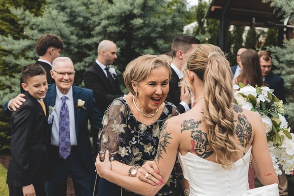 An older woman joyfully embracing the bride immediately after the ceremony outdoors, surrounded by family and friends
