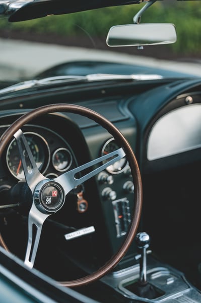 Interior dashboard of a classic convertible Corvette viewed from above, showing the wood-rimmed steering wheel and analog gauges