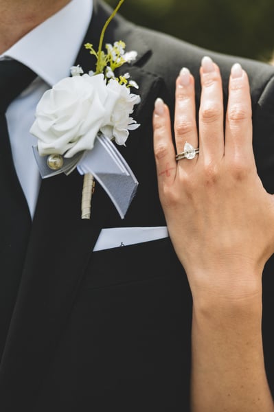 Close-up of the bride's pear-cut diamond ring displayed against the groom's boutonniere on his lapel