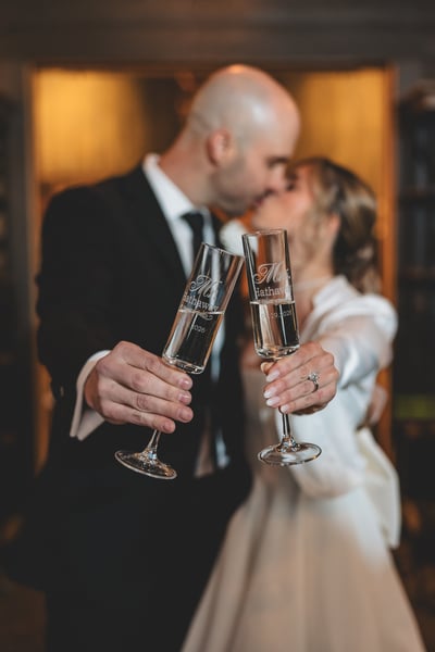 Bride in her white mini reception dress and blazer dancing with a drink in hand inside the warmly lit barn reception space