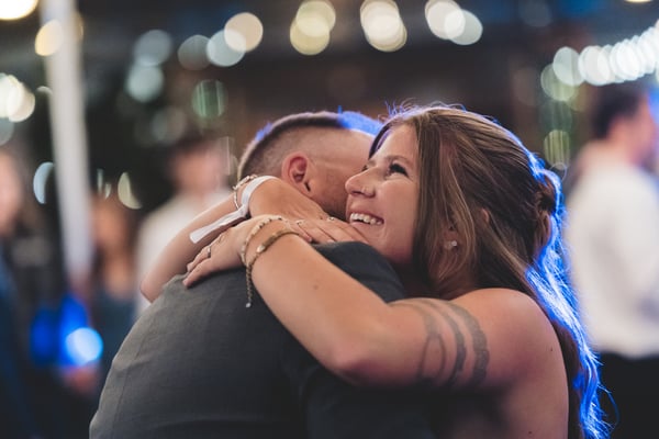 Bride and groom embracing beneath a lush green-lit archway at night, she in her white mini dress and platform Converse shoes