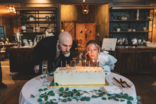 Bride and groom kissing while holding up their Mr. and Mrs. Hathaway engraved champagne flutes toward the camera in a warm indoor reception space
