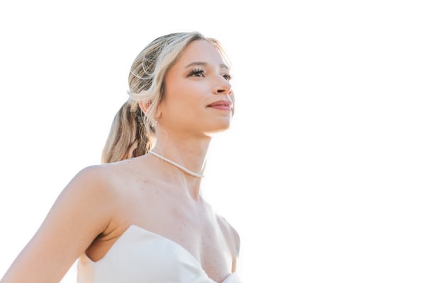 Close-up portrait of bride looking upward with a soft smile, pearl choker catching the bright overexposed sunlight, earring visible