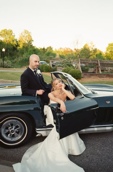Groom perched on the Corvette at golden hour while bride leans out the car door looking up at him