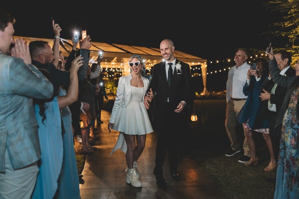 Groom dipping the bride for a dramatic nighttime kiss during the sparkler send-off, surrounded by guests in the parking lot