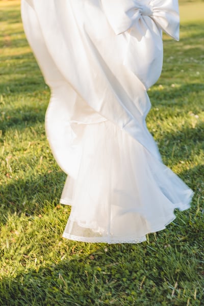 Detail shot of the mermaid gown bow and lower train flowing across green grass in afternoon light
