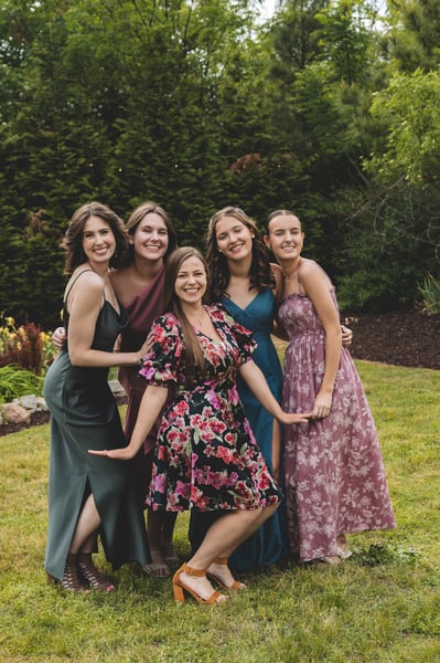 Group of five female guests in colorful and floral dresses posing together and laughing on the garden lawn