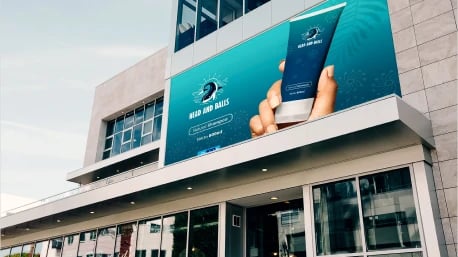 Exterior of a modern building with a large promotional banner displaying a hand holding a mobile phone, advertising 'Aqua and Bubs' as a water delivery service, set against a clear sky.