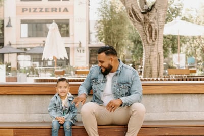 Latino father and young son sitting together outside, reflecting family support and connection