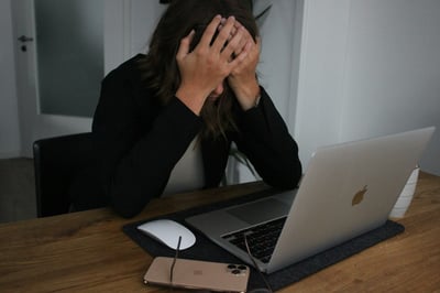 Stressed woman holding her head in front of a laptop, symbolizing overwhelm and the need for stress management support