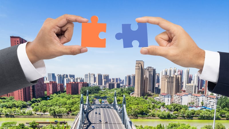 Two hands holding puzzle pieces, symbolizing M&A success over a bridge with a city in the background.