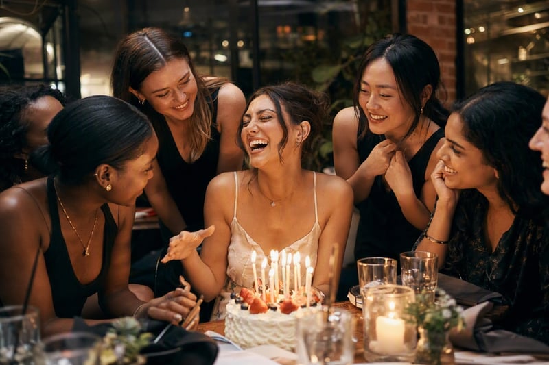 Friends leaning in around a lit birthday cake, shot with a hard flash