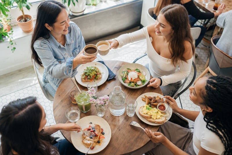 A long brunch table in window light with coffee, pastries and half-eaten plates