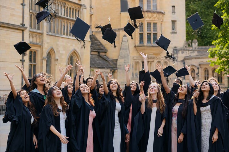 Graduates in gowns throwing caps in the air outside a stone university building