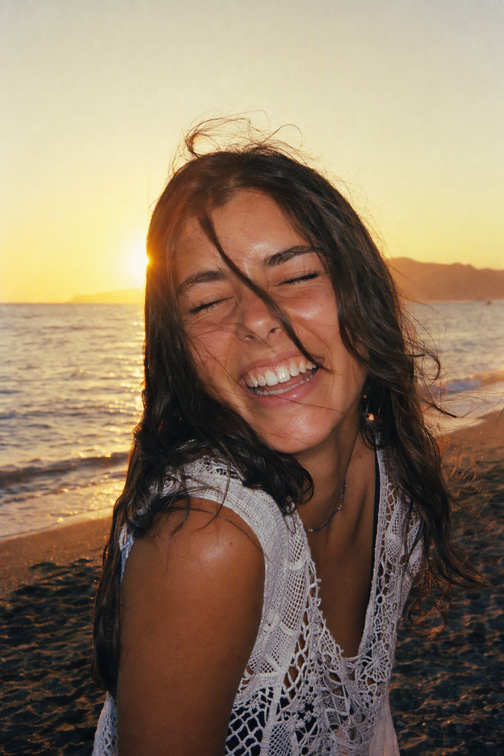 Woman laughing on a beach at golden hour, disposable camera look