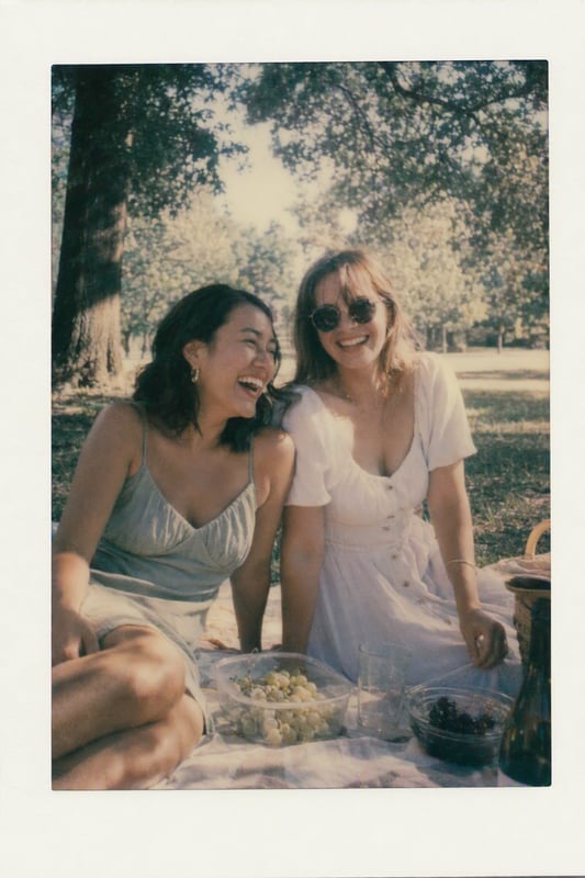 Two friends laughing at a picnic, soft faded instant-film colours