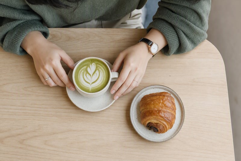 A matcha latte and a paperback on a pale table beside a bright window