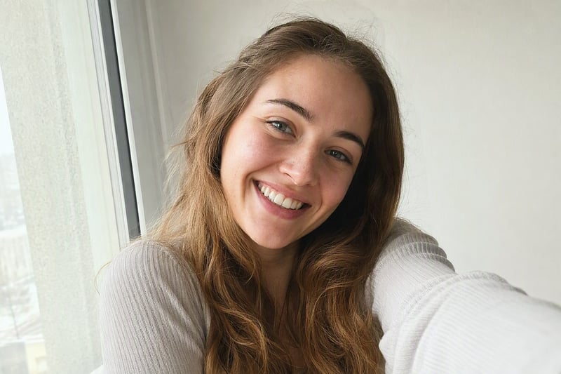 Woman taking a selfie beside a window in soft daylight, no heavy retouching
