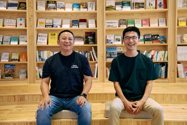 書棚に囲まれたスペースで笑顔を見せるKOBIRAのメンバー2人