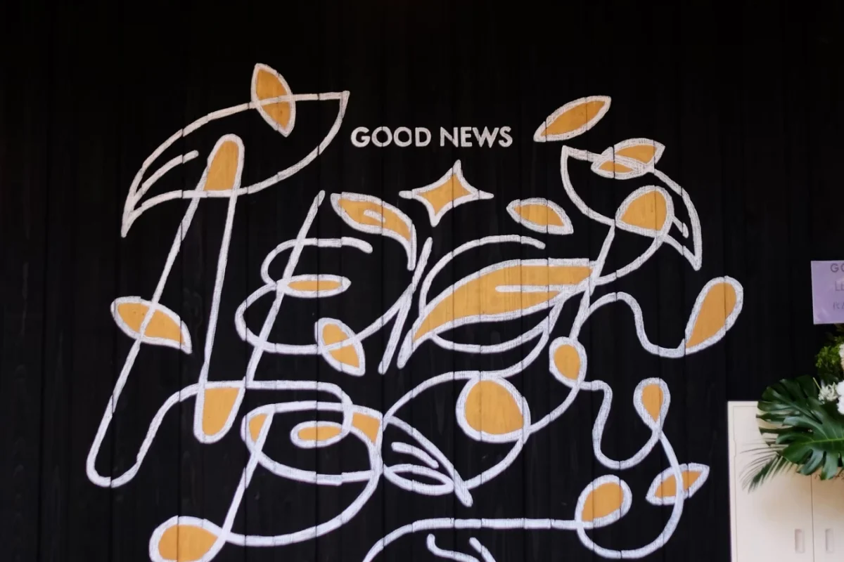 黒い板壁に描かれたGOOD NEWSのロゴと手描き風のレタリング