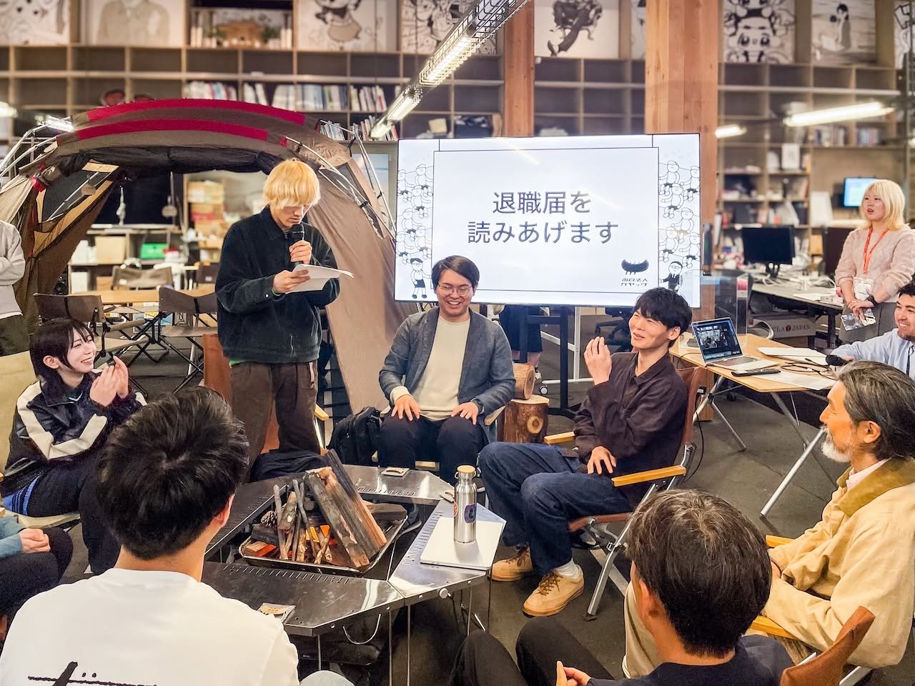 室内の焚き火を囲み、マイクで文章を読み上げる人を見守る参加者たち
