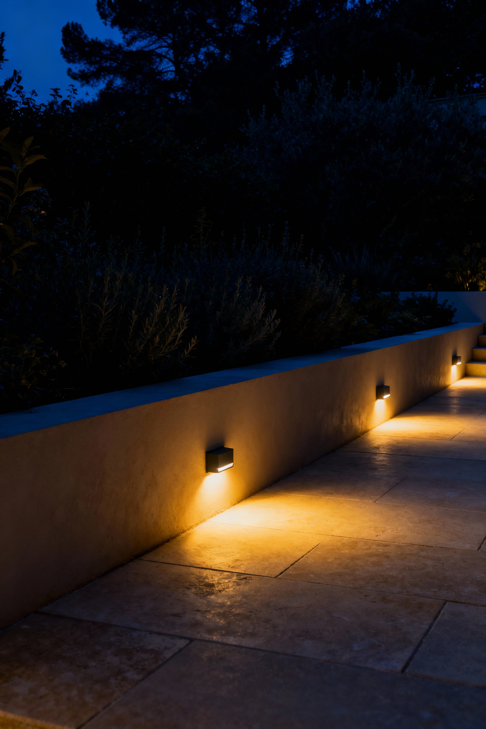 A photograph showing a luxury garden path at night illuminated solely by low-impact, fully-shielded 2700 Kelvin warm LED lighting that respects the dark sky and nocturnal environment.