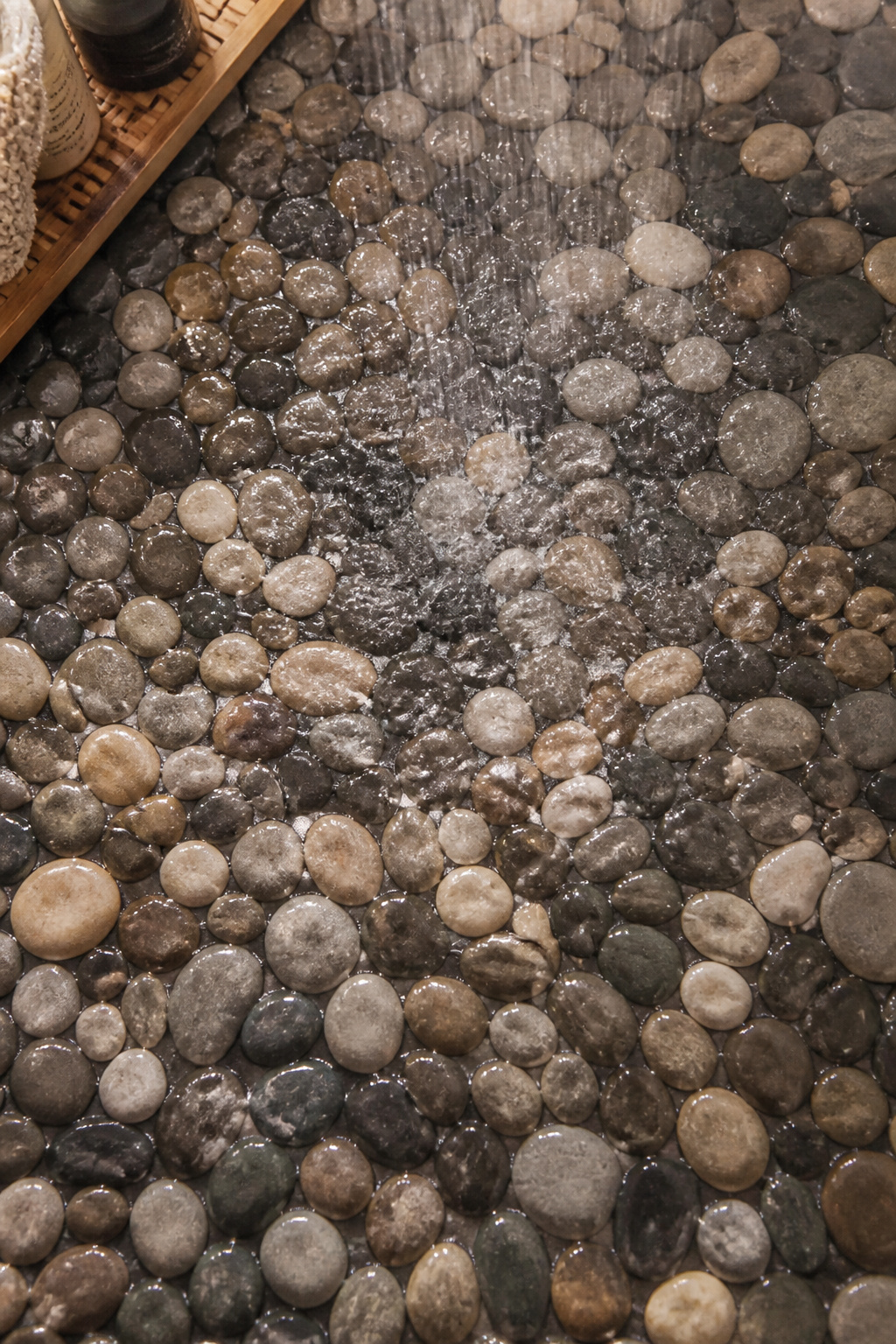 Natural river pebble tile on a shower floor — wet, glistening, and providing the kind of barefoot tactile experience that flat tile cannot offer.