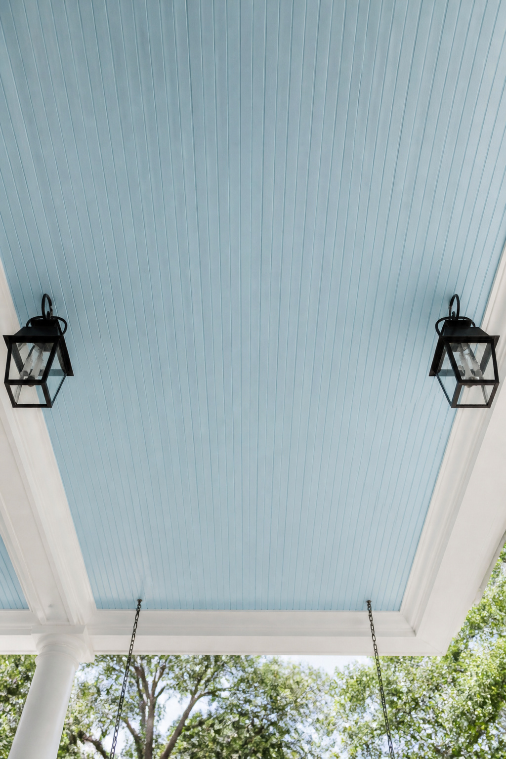 Haint blue beadboard — pale and sky-like overhead — creates a canopy effect that makes the porch feel simultaneously open and protected.