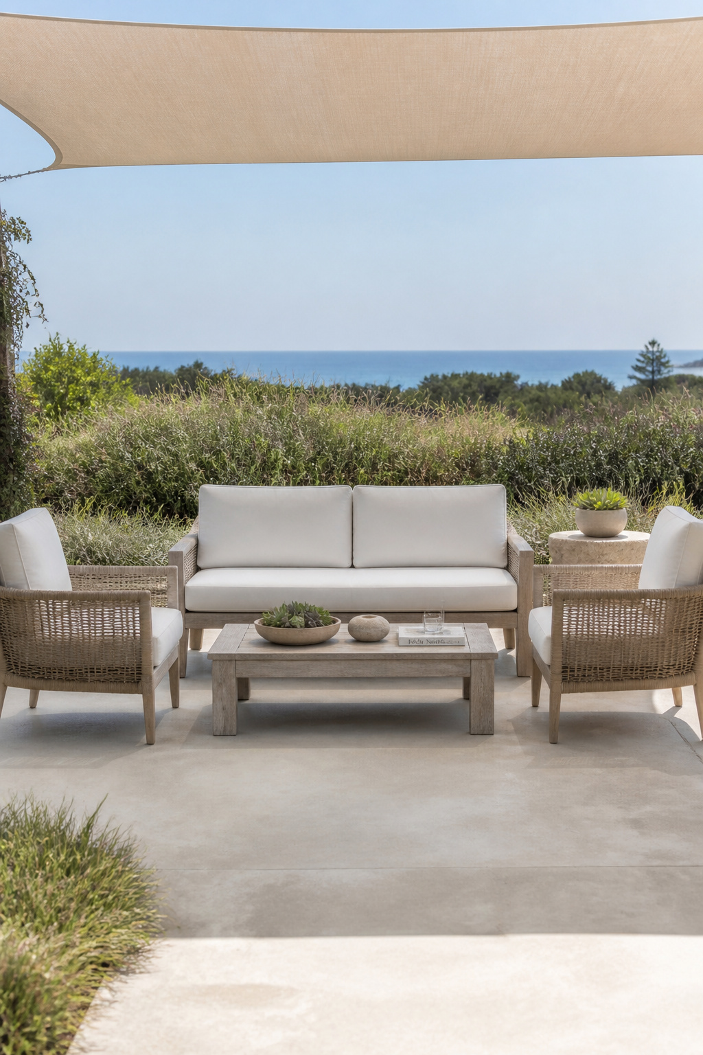 Grade A teak furniture silvered to a natural grey patina pairs with PE synthetic wicker armchairs and linen-white cushions on a coastal contemporary patio — restraint and quality as the complete design statement.