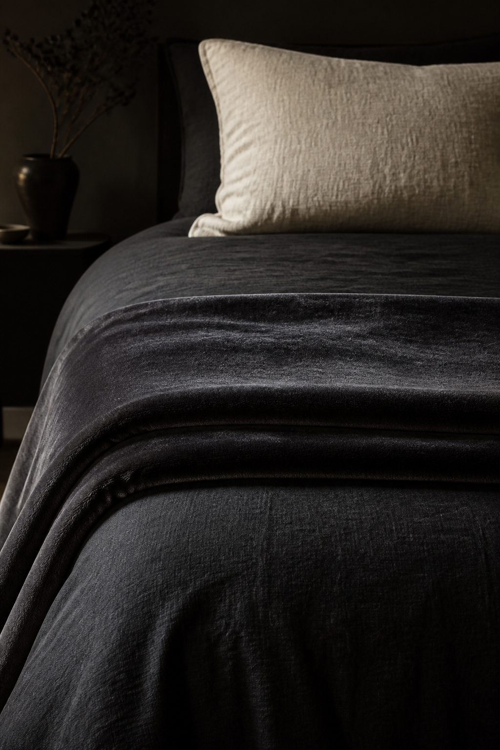 A charcoal velvet throw over matte black linen creates tonal movement within a single palette — velvet's pile catches and shifts the light throughout the day in a way flat fabric cannot.