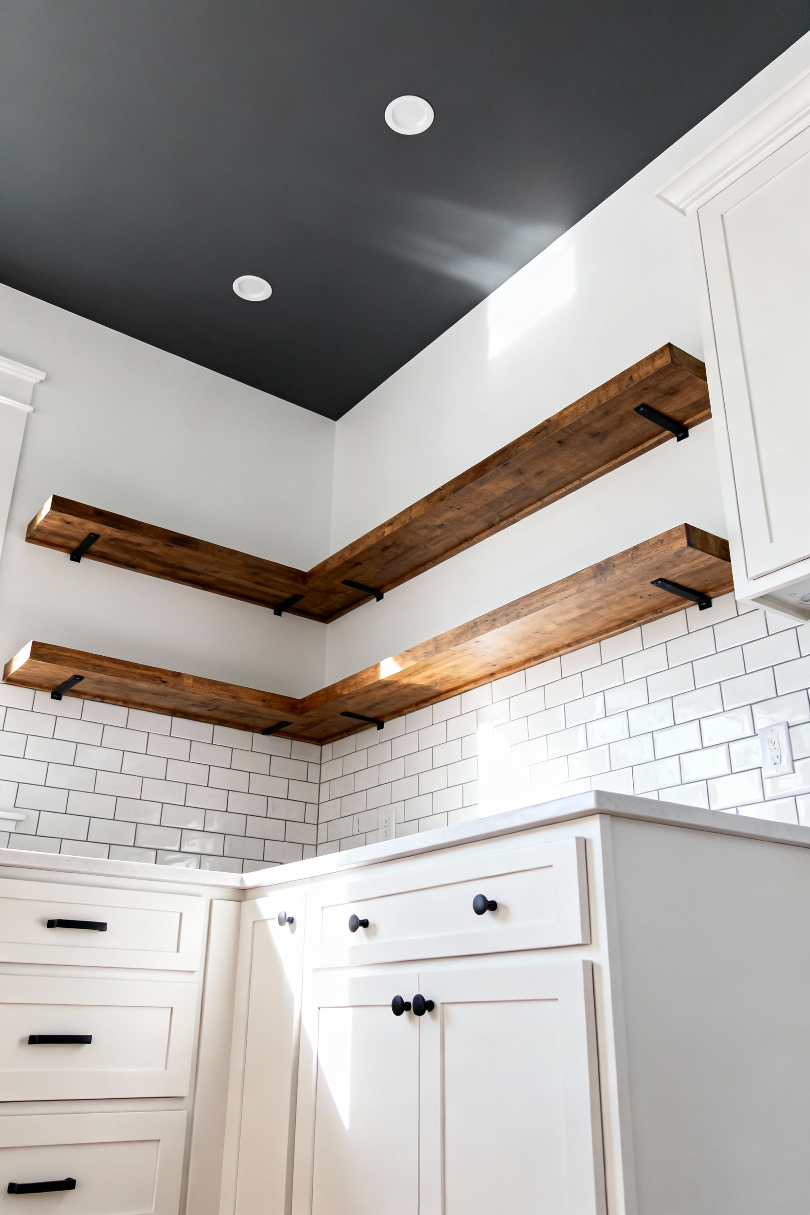 A modern transitional kitchen utilizing budget-friendly design tricks, featuring a deep matte charcoal painted ceiling that visually expands the room's height, contrasting with crisp white walls and simple wooden open shelving.