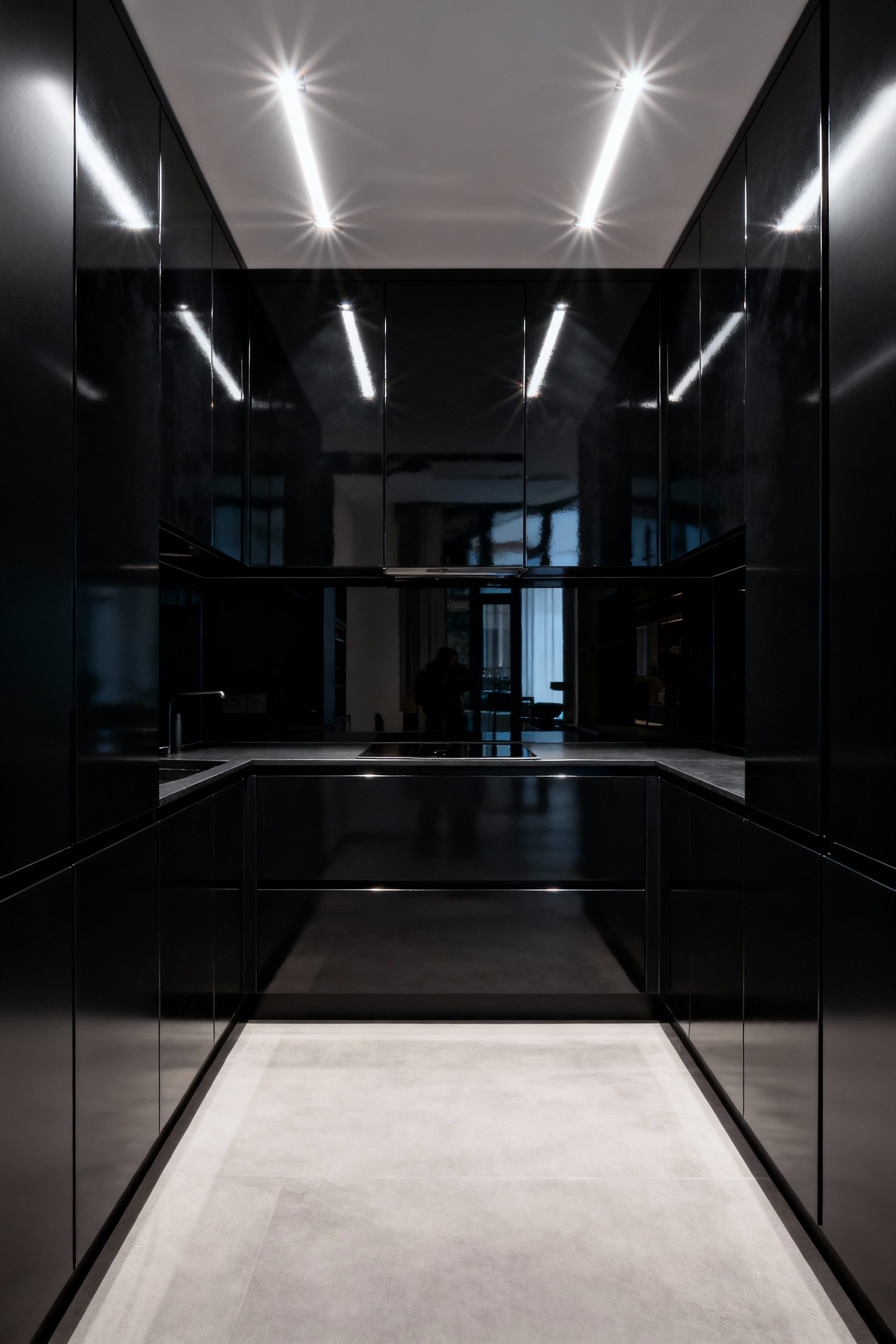 High-gloss black kitchen cabinets displaying intense specular reflection from overhead recessed downlights, showing sharp glare points and the reflected expansion of the small, modern kitchen space.
