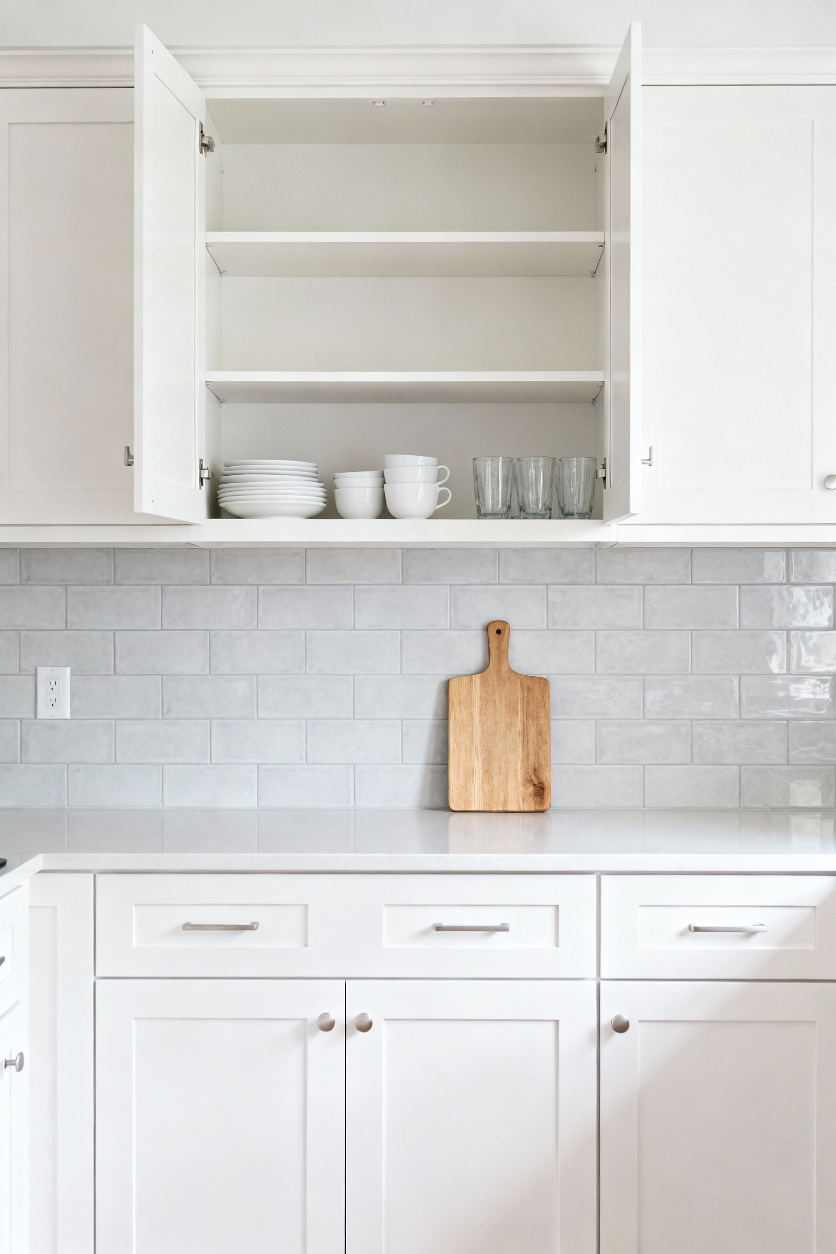 Detailed photograph showing a clever kitchen remodel on a budget where upper cabinet doors were removed and the interior shelving was styled with white dishes to create airy open shelving, emphasizing the concept of negative space.