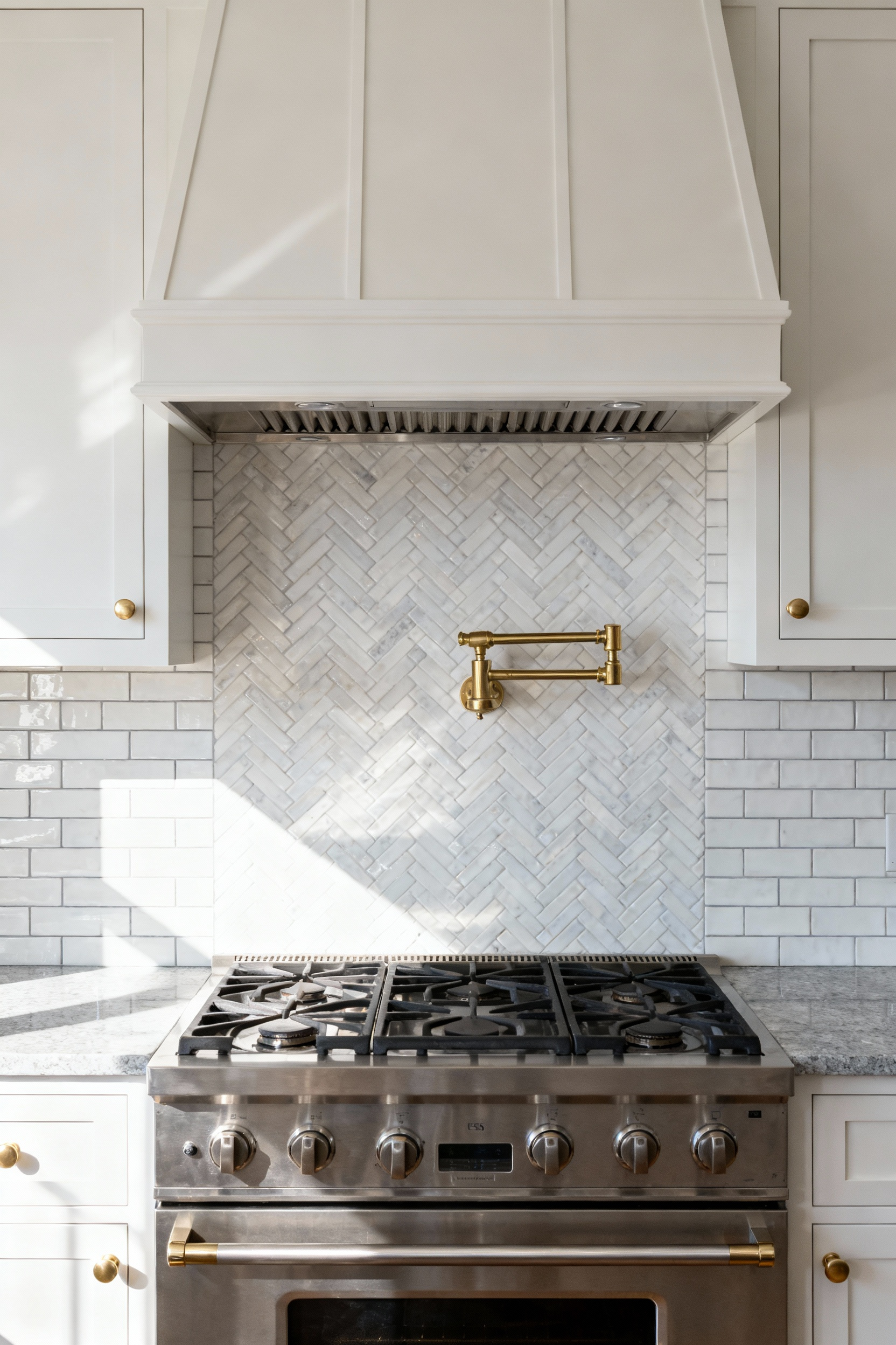 A monochromatic white kitchen backsplash where subway tile on the perimeter transitions into a herringbone pattern behind the stainless steel range, demonstrating texture as a subtle focal point.