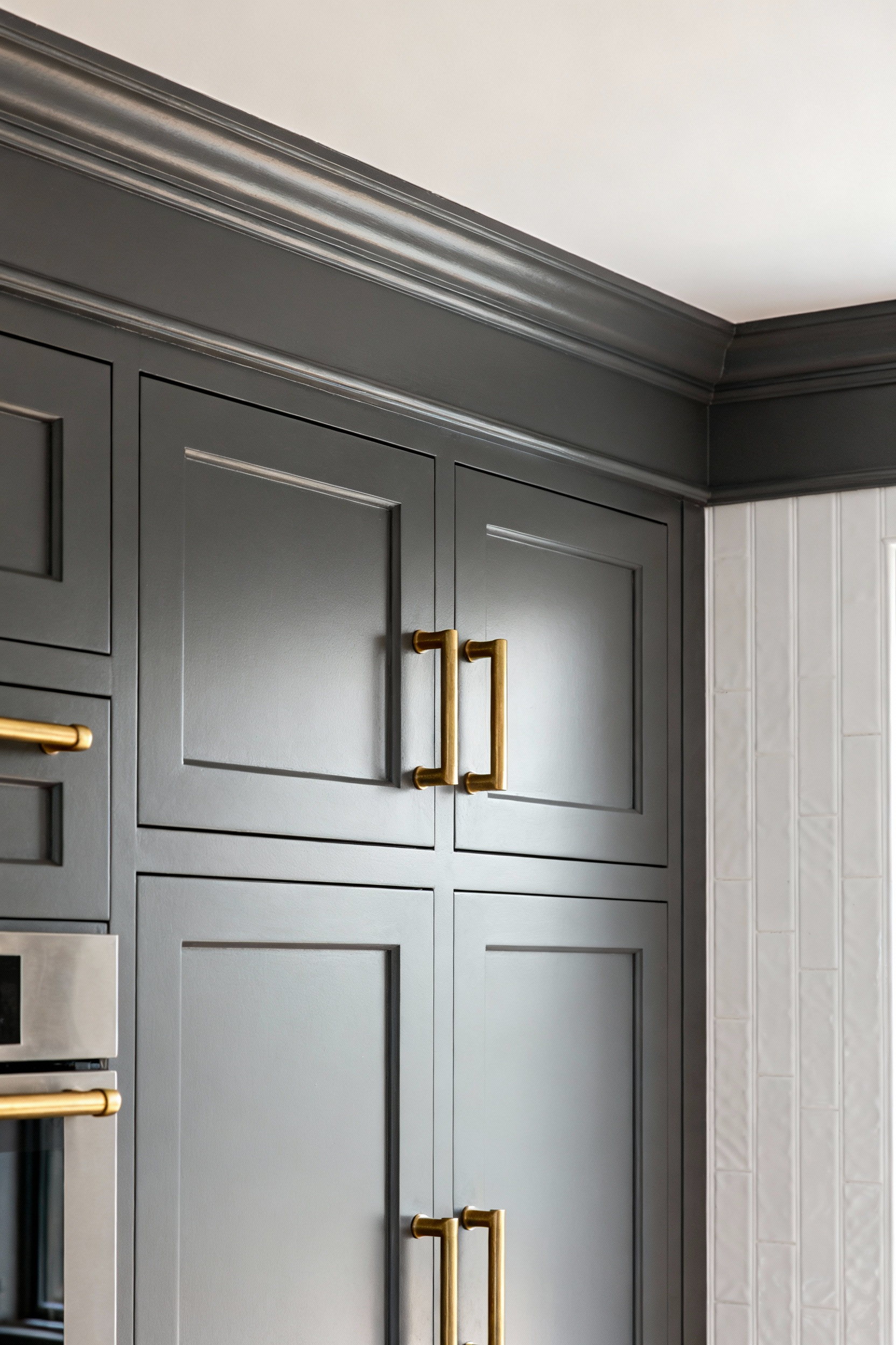 Seamless, custom-look kitchen cabinetry achieved by adding painted crown molding to stock cabinets, paired with high-end solid brass hardware, illustrating a designer upgrade on a budget.