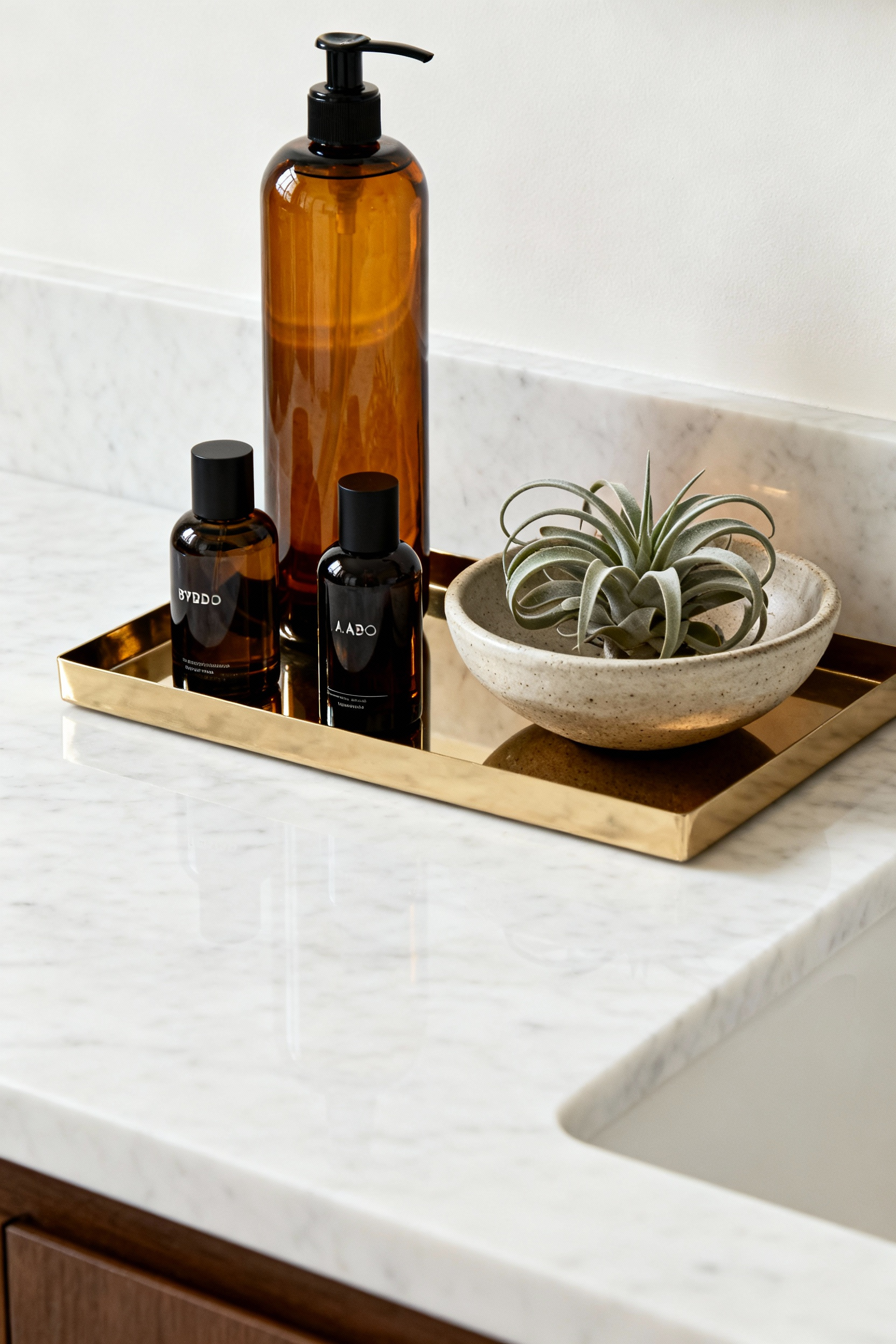 Close-up of a luxury bathroom apothecary vignette on a marble vanity, featuring amber glass bottles, polished brass tray, and a sculptural plant.