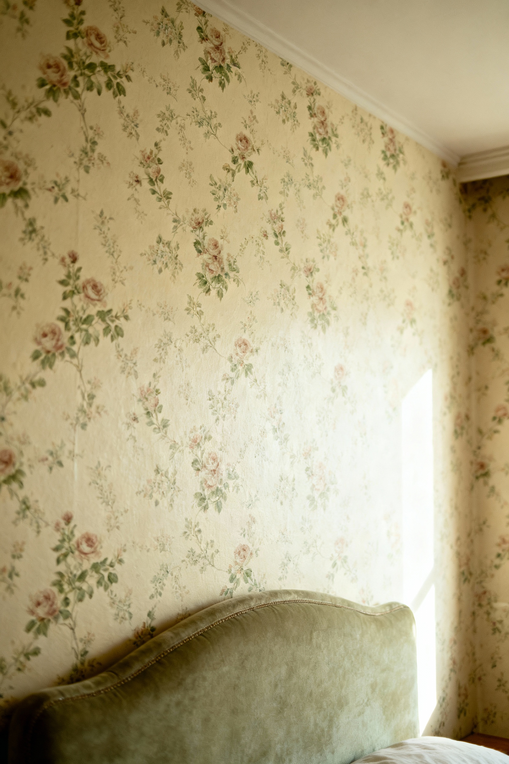 A vintage bedroom featuring an accent wall with cream-colored floral wallpaper, showcasing delicate rose patterns. A classic headboard and soft lighting contribute to a serene, timeless aesthetic.