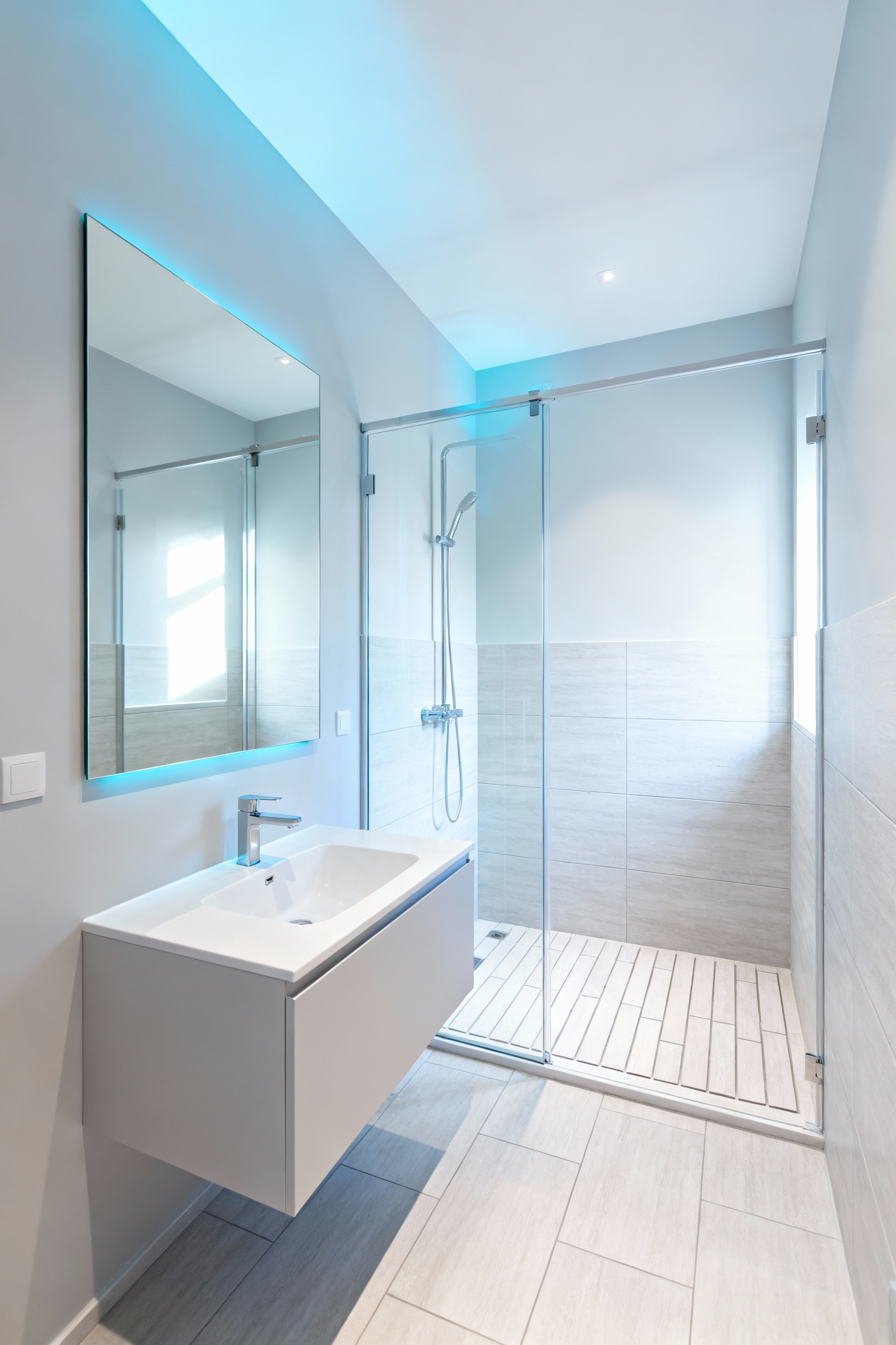 A modern small bathroom interior featuring walls painted in a very light, reflective grey. The room includes a minimalist floating vanity, a large frameless mirror, and a clear glass shower, all contributing to a bright and spacious appearance, showcasing how light paint visually expands the walls.