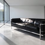 A modern minimalist living room featuring a black leather Le Corbusier style sofa with a visible chrome steel frame as the architectural centerpiece.