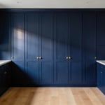 A modern high-end kitchen featuring floor-to-ceiling navy blue cabinetry and white marble countertops showing the impact of bold kitchen cabinet colors.