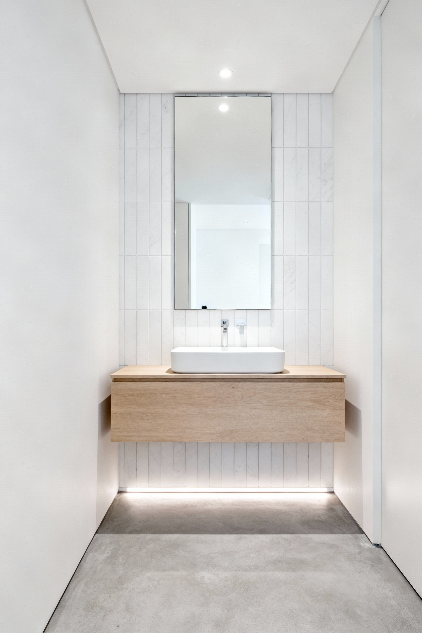 A modern, compact bathroom featuring a sleek light wood floating vanity installed over continuous polished concrete flooring, creating the illusion of deep, expanded space.