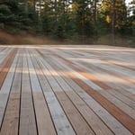 A wide cedar deck showing a weathered silvery-gray patina transitioning from the original warm reddish-brown wood color, set in a natural forest environment.